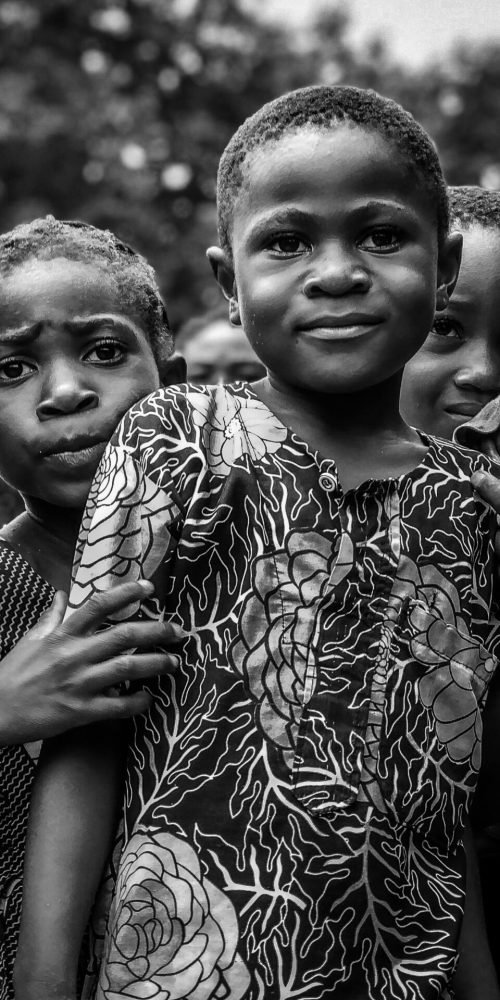 Heartwarming black and white photo of smiling African children standing together in an outdoor setting.