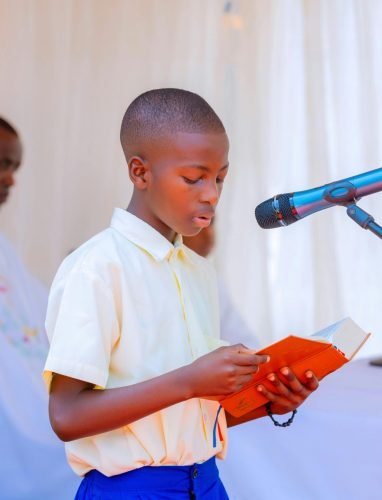 A young boy reads from a religious text during a ceremony with a priest nearby.